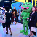 Attendees at Dubai’s Token2049 conference pause for a picture with a mascot for meme coin Pepe the frog on Wednesday. (Giuseppe Cacace /AFP via Getty Images)