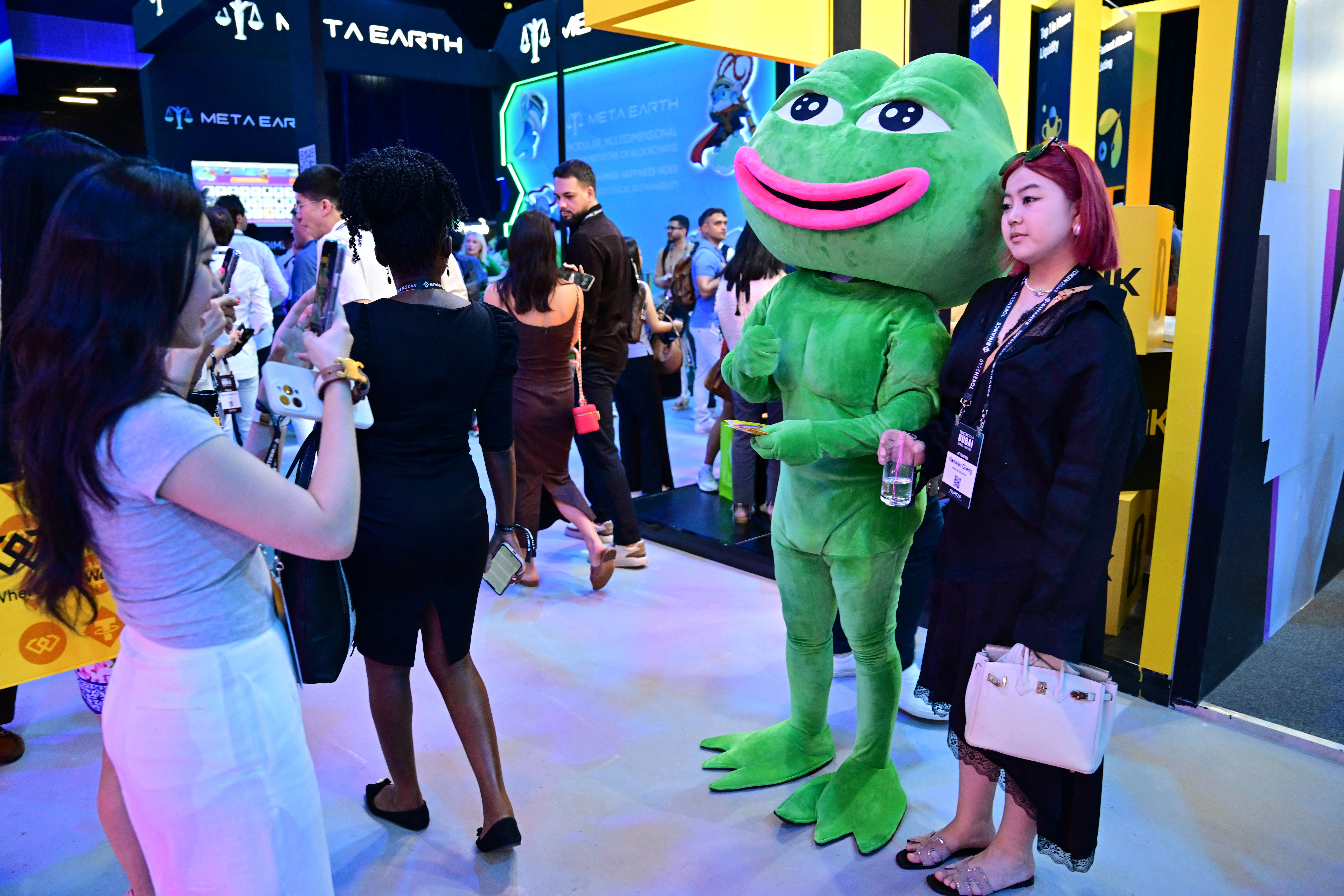 Attendees at Dubai’s Token2049 conference pause for a picture with a mascot for meme coin Pepe the frog on Wednesday. (Giuseppe Cacace /AFP via Getty Images)