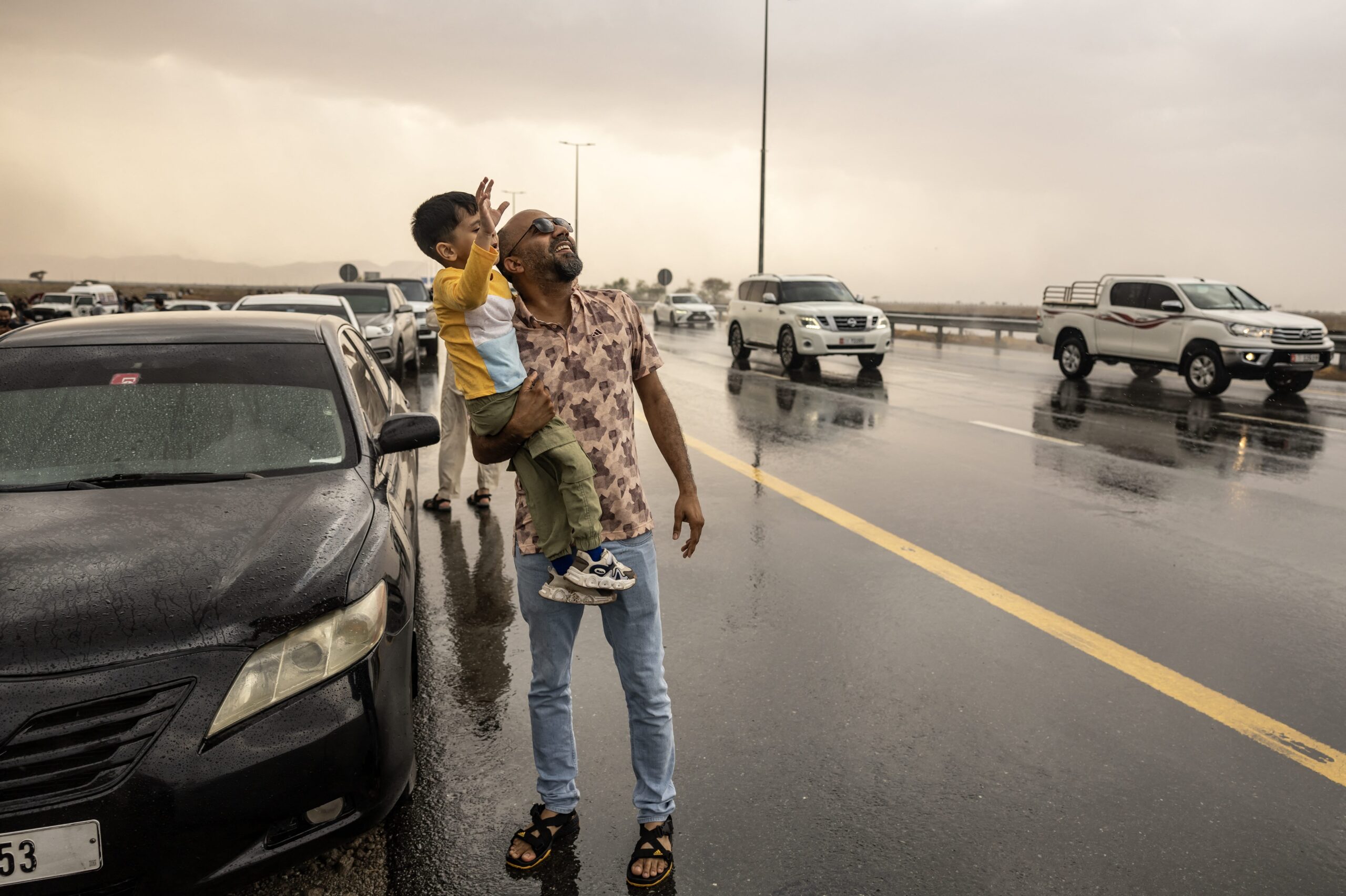 A man holds his child as people stand in the rain during a "rain chase" in the emirate of Sharjah on Saturday. The UAE experiences so little rainfall that “chasing” rain has become a niche hobby for some residents, who have taken to following Muhammed Sajjad, known as "The Weatherman,” as he finds the best places to enjoy the rare occasion of wet weather. (Fadel Senna/AFP via Getty Images)